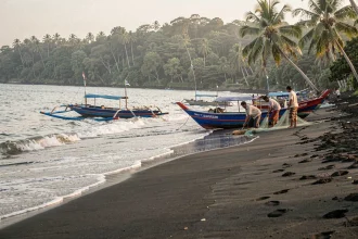 Plage de sable noir de Lovina à Bali avec des bateaux de pêche traditionnels Jukung colorés au bord de l'eau au lever du jour